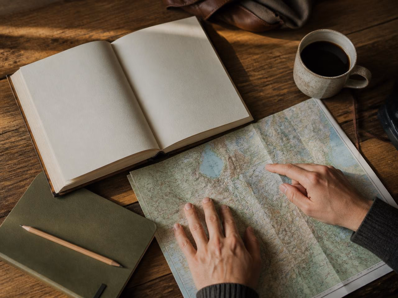 Mesa de madeira com livro aberto, mapa e caderno durante o planejamento de uma viagem.